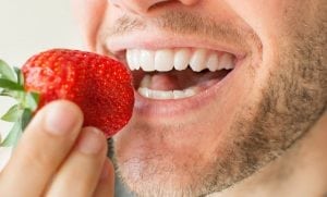 A man eats a strawberry that contains acids to whiten teeth